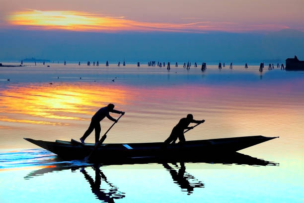 Venice sunset silhouette of sinchronized rowing men stock photo