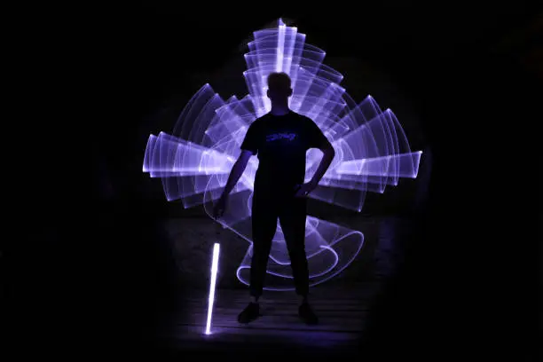 Boy standing with a lightsaber with neon drawings and leds at lightpainting. Inscription "escape" on t-shirt.