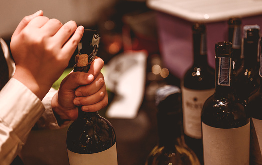 The bartender opens a bottle of red wine using a wine opener. To pour a lot of empty glasses at the bar counter. Blurred background. wine, tasting, open, beverage, bartender, dinner concept.