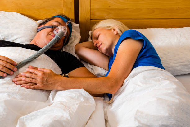 istock man using cpap mask because of obstructive sleep apnea, his wife is beside 1263376665