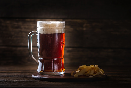 A glass of wheat dark beer with foam on the table on wooden background