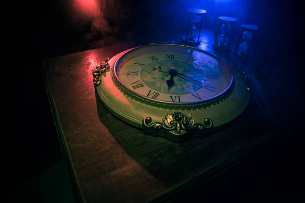 istock Time concept. Big vintage round clock on wooden table with abstract light. 1263381136