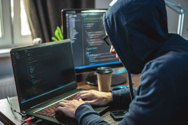 Hacker in the hood is programming virus code at the keyboard for the laptop. Internet fraud and personal data hacking stock photo