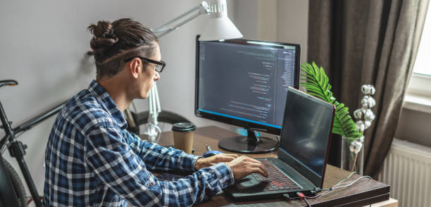 Male programmer is writing program code on a laptop at home. The concept of software development stock photo