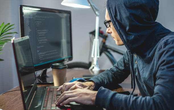 Hacker in a hood are programming virus code on a laptop. The concept of Internet fraud and personal data hacking stock photo