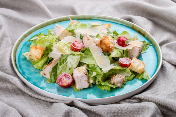 salada caesar com frango, parmesão e tomate cereja. em uma placa azul em um fundo têxtil - food and drink cheese grated bowl - fotografias e filmes do acervo