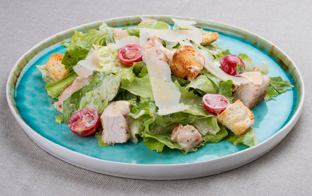 salada caesar com frango, parmesão e tomate cereja. em uma placa azul em um fundo têxtil - food and drink cheese grated bowl - fotografias e filmes do acervo