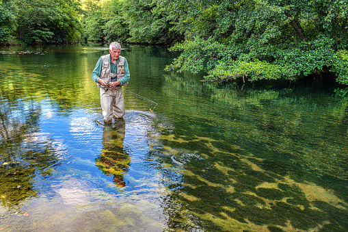 Pitlochry, Scotland - September 13, 2022: Scottish Fly fisherman stands quietly as he leaves his fly to lie for Salmon in the turbulent waters of the River Tummel