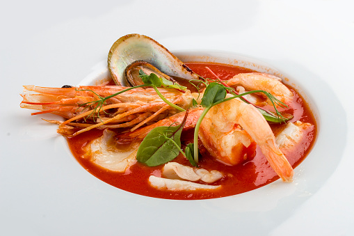 French bouillabaisse fish soup with shrimp, mussels and scallop. In a white plate on a textile background