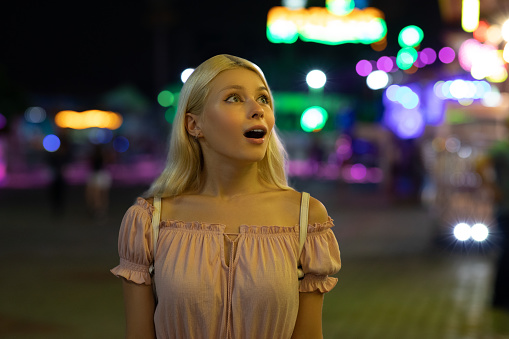 Teenagers enjoying amusement park weekend closeup. Smiling two friends walking illuminated street talking on summer night. Beautiful girls rest carnival holding eating snacks. Holiday leisure concept