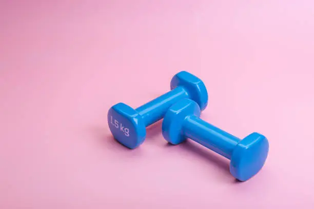 Photo of A pair of blue dumbbells on a pink background