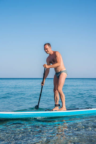 istock Fit Middle Aged Man Paddle Boarding by the Coast 1263413589