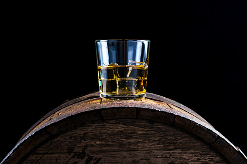 A glass of whiskey and ice cubes on an old wooden barrel