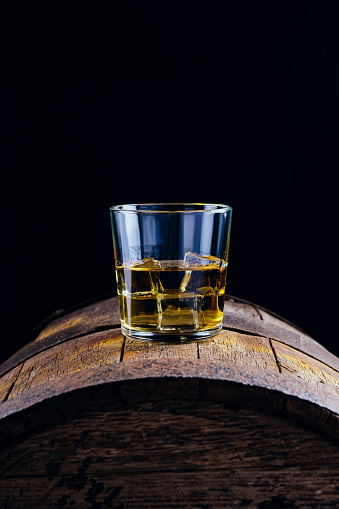 A glass of whiskey and ice cubes on an old wooden barrel