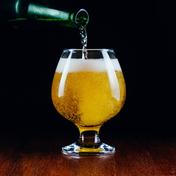 istock Lager beer pours from a bottle into a glass on a black background 1263421126