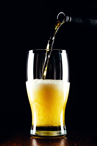 Lager beer pours from a bottle into a glass on a black background