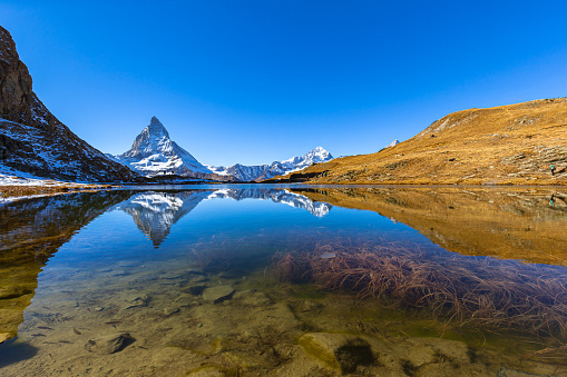 Stunning panorama view of the famous Matterhorn and Weisshorn peak of Swiss Pennine Alps with beautiful reflection in Riffelsee lake on sunny autumn near train station Riffelberg, Valais, Switzerland
