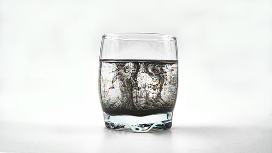 Isolated glass of water with black ink on the white background, manipulation with ink on glass.