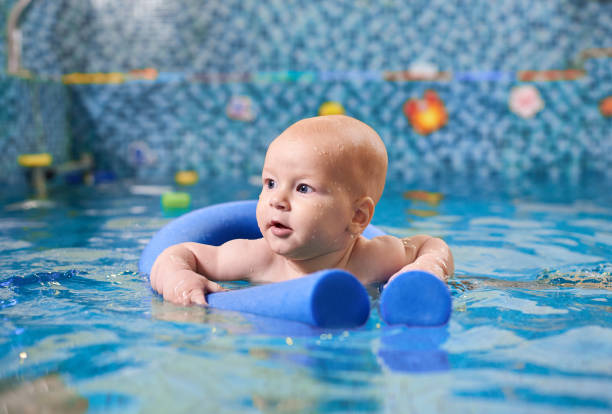 adorable niño nadando en la piscina con fideos en la piscina. - bebe bañandose fotografías e imágenes de stock