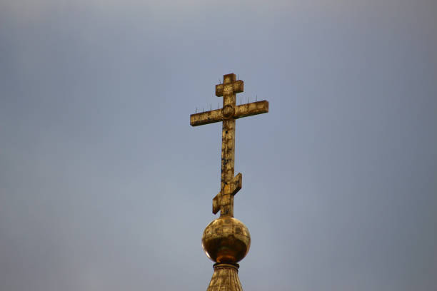 old gilded christian orthodox cross over a temple against a cloudy sky