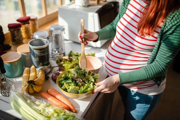 Healthy pregnant woman preapring a fresh organic salad for her breakfast Happy eight month pregnant woman with red dyed hair making a healthy vegan salad in her modern kitchen dyed red hair photos stock pictures, royalty-free photos & images