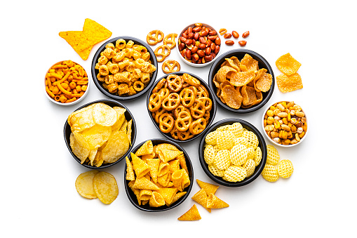Party food: assortment of salty snacks in bowls shot from above on white background. Predominant colors are yellow and white. High resolution 42Mp studio digital capture taken with SONY A7rII and Zeiss Batis 40mm F2.0 CF lens