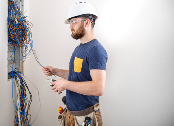 istock Electrician Builder at work, examines the cable connection in the electrical line in the fuselage of an industrial switchboard. Professional in overalls with an electrician's tool. 1263444017