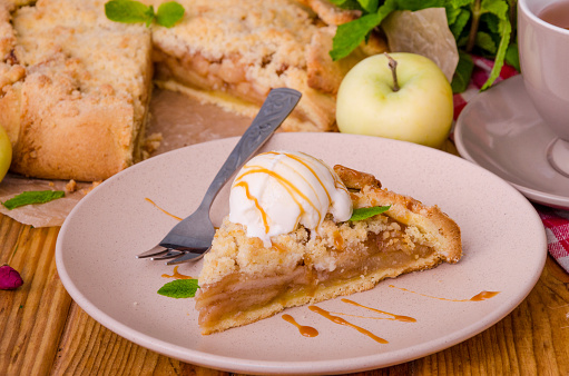 Open pie or galette with apples with cinnamon and crumbs served with a cup of hot tea and a scoop of vanilla ice cream.