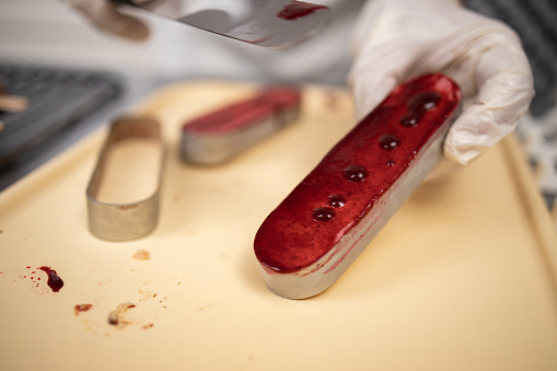 Chef covering chocolate biscuit with raspberry jam,wearing protective gloves