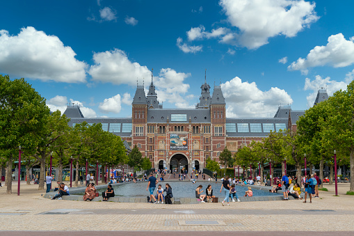 Amsterdam, The Netherlands - 23th July 2020 - Tourists sitting on the edge of the pond in front of the Rijksmuseum (federal museum) in the center of Amsterdam
