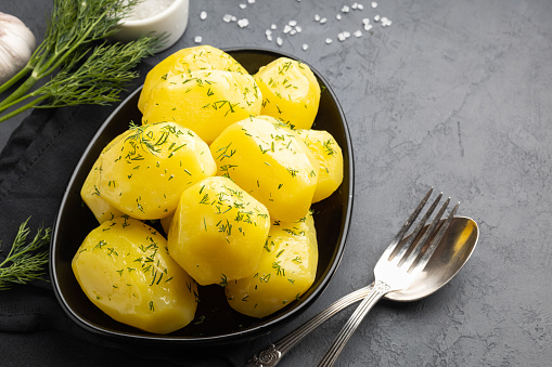 Delicious boiled potatoes with dill in a black plate.