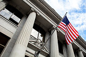 American flag flying over government building in city, blue sky and clouds