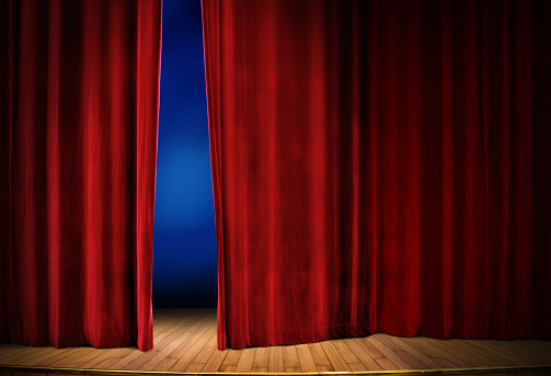 close up red stage curtain opening over wooden floor stage