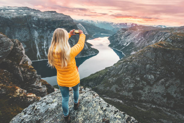 mujer tomando fotos por teléfono inteligente en el acantilado de la montaña sobre el lago viajando en noruega aventura estilo de vida vacaciones activas concepto de conexión de tecnología moderna - noruega fotos fotografías e imágenes de stock