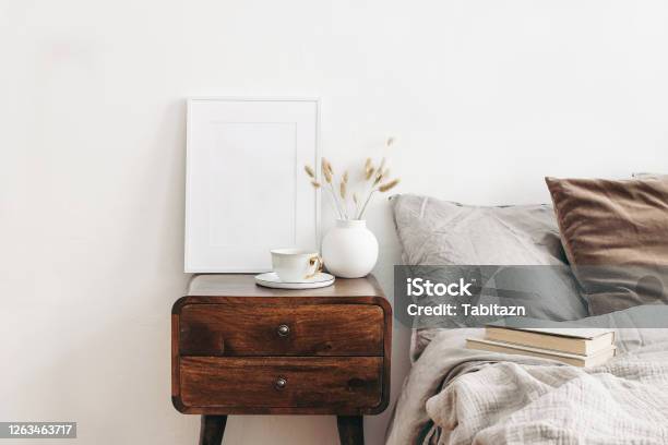 Portrait White Frame Mockup On Retro Wooden Bedside Table Modern White Ceramic Vase With Dry Lagurus Ovatus Grass And Cup Of Coffee Beige Linen And Velvet Pillows In Bedroom Scandinavian Interior Stock Photo - Download Image Now