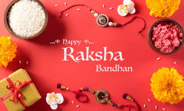 Raksha Bandhan, Indian festival with beautiful Rakhi and  Rice Grains on red background.  A traditional Indian wrist band which is a symbol of love between Sisters and Brothers.