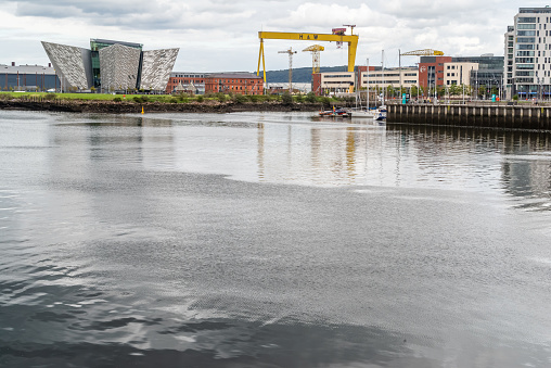 Belfast, Northern Ireland, United Kingdom - August 1, 2020: View across the River Lagan towards the Titanic Quarter, featuring the Titanic Museum, Titanic Hotel, Belfast Metropolitan College ('The Met') and the cranes of Harland and Wolff (shipyard).