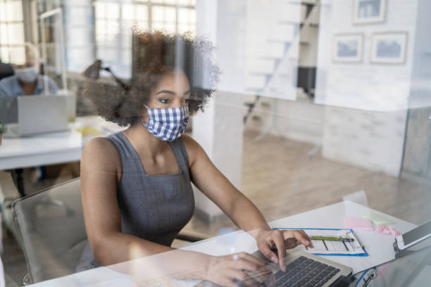 Through the acrylic glass in the office African businesswoman working in office behind acrylic glass form maintaining social distancing office cubicle mask stock pictures, royalty-free photos & images