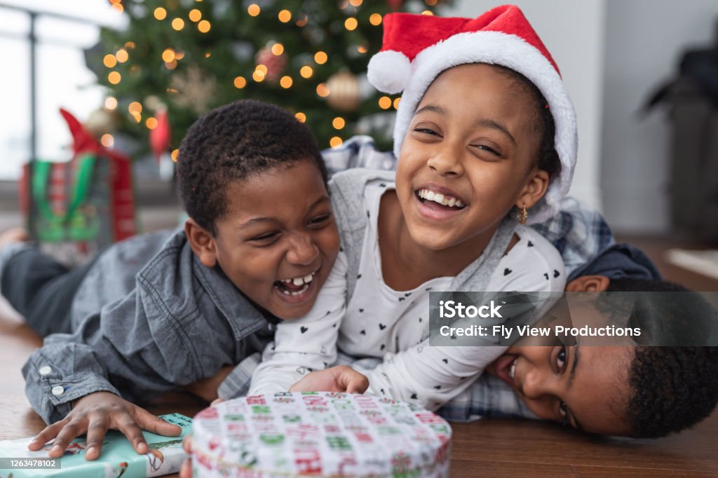 Sibling fun on Christmas Day Three (3) siblings of African American descent enjoy Christmas Day together. They are laughing and laying on top of each other. Child Stock Photo