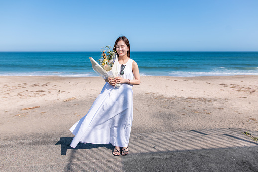 Portrait of young woman standing on summer beach, holding bouquet