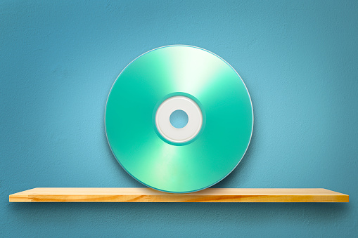 Blank music CD on wooden shelf against blue wall with copy space.