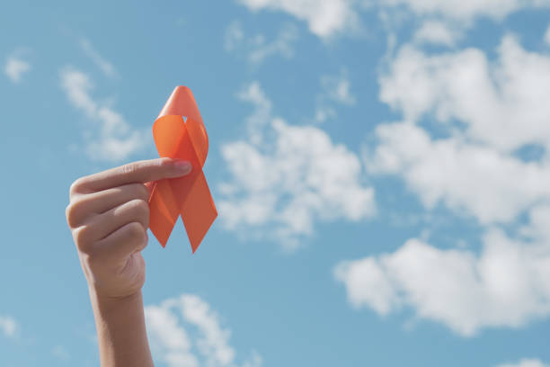 hands holding orange ribbon over blue sky, leukemia cancer and multiple sclerosis, copd and adhd awareness, world kidney day - esclerose múltipla imagens e fotografias de stock