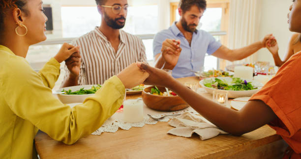 Don’t forget your friends when you count your blessings Shot of a group of young friends praying before sharing a meal together at home saying grace stock pictures, royalty-free photos & images