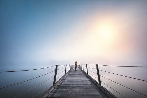 Woman standing on the bridge on a foggy winter day. Sun is breaking through the mist.