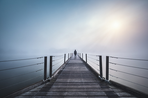 Man standing on the bridge on a foggy winter day. Sun is breaking through the mist.