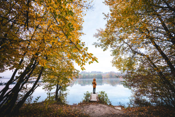 Idyllic autumn scene with woman standing on the wooden jetty by the lake.
