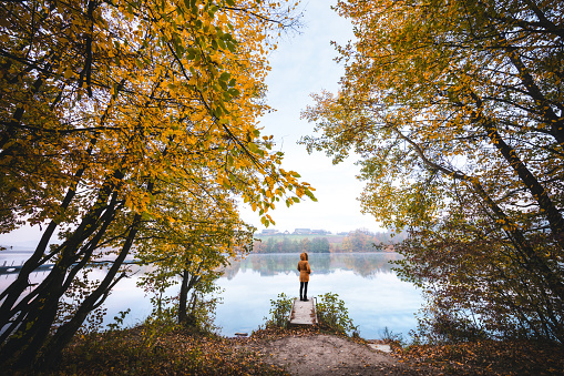 Idyllic autumn scene with woman standing on the wooden jetty by the lake.