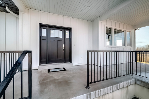 Home entrance with front porch and black front door against white panelled wall. Stairs leads to the entrance of this house with glass panes on the door.