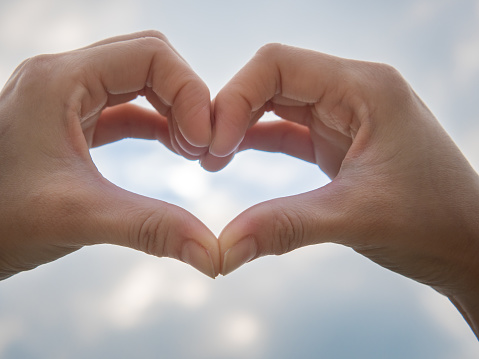 Heart symbol from hands on the blue sky background, Concept for Love or Health.