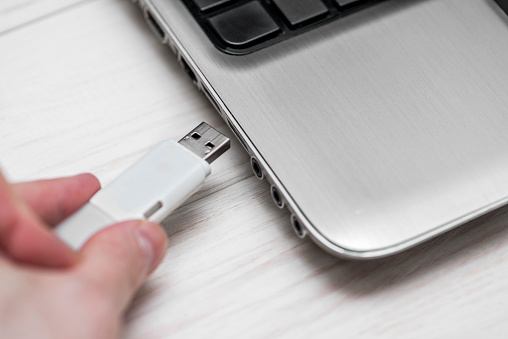 Plugging removable flash disk memory into laptop USB slot. Man hand inserting USB flash drive into laptop computer on wooden white background. Copying data from flash drive to laptop computer